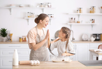 Happy woman and her little daughter cooking in kitchen