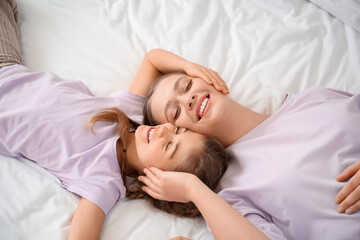 Happy woman and her little daughter lying on bed, top view