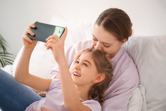 Happy woman and her little daughter taking selfie in bedroom