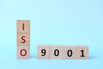 ISO 9001 or Quality Management Systems concept on wooden blocks in blue background.	