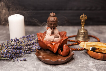 Buddha figurine and smoky incense with candle, bell and rosary. Aromatherapy and spa. Buddha statue with candle burning and incense smoke. Religious concept. Buddha figurine with incense smoke.