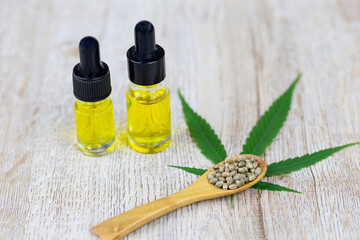 Cannabis seeds in a wooden spoon are placed on top of the cannabis leaves. Oil extracted in a glass bottle. The idea of extracting hemp oil is a natural drug. The idea of planting seeds is seedlings.