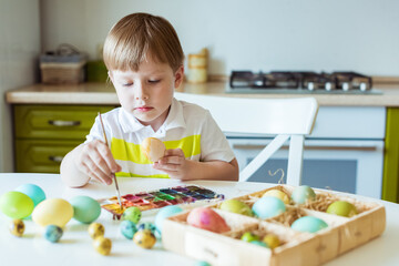 Caucasian boy paints Easter eggs with paints and brush. Preparing for Easter holiday