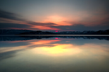 Fototapeta na wymiar 雲の向こうに陽の沈む空を水面に映す黄昏の湖。日本の北海道の屈斜路湖。