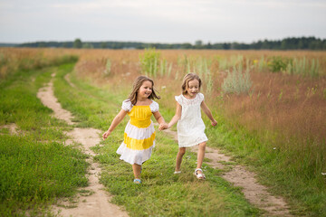 Naklejka na ściany i meble Emotional sisters running on the road through the field, the concept of freedom, happiness and childhood, lifestyle, summer
