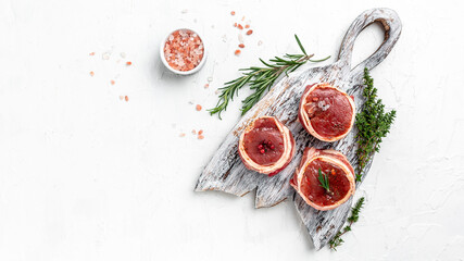 Fresh pieces pork ready to cook. Sirloin medallions steaks wrapped in bacon on woden board on a light background, filet Mignon. top view