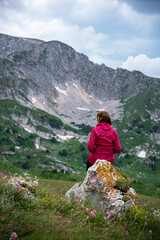 Naklejka na ściany i meble A women in a red jacket sits on a rock in a mountain valley and looks into the distance. Mountain landscape. Russia, Adygea