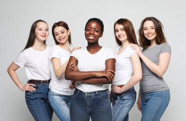 Group of happy young women of different size and ethnicity in t-shirts over grey background