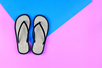 Top or above view / flat lay of flip-flop sandal, open-toed shoe on pink blue background : Light shoe made of dried grass, eco-friendly footwear with black straps attaching the rubber sole to the foot