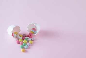 Eggshells with colorful chocolate candies Copy space on pink background. Creative minimal Easter holiday concept.