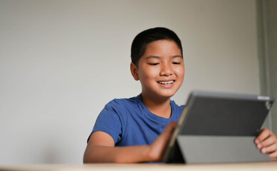 close up young asian boy playing on digital tablet device to watch entertainment media or video call with friends and family during home quarantine for education and technology concept
