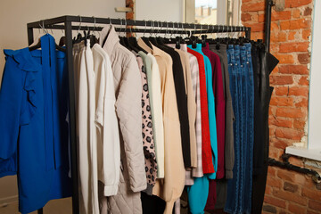 Interior of showroom with stylish clothes. Wardrobe rack with stylish clothes near brick wall and window indoors. Details of bright beauty colored dress collection in show room. Copy space for text