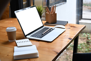 Comfortable workplace with computer laptop, notebook, coffee cup and pencil holder on wooden table.