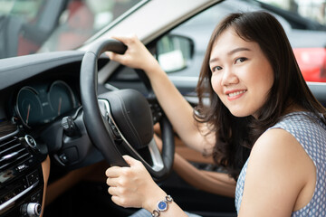 Fototapeta na wymiar Happy Asian young woman driver sitting on the driver seat in the luxury modern car