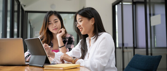 Horizontal photo of two female college student working on digital tablet and  talking about lessons comparing together.