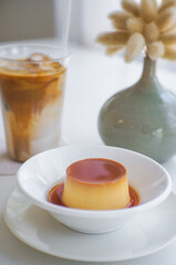 Caramel pudding in white plate and Iced coffee latte is freshly drank in a glass on a white table