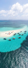 Obraz premium View from above or from a bird's eye view of the coral island, the white sand beach and the beautiful, clear turquoise waves with boats.