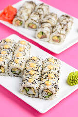Sushi large set served on a white plate over pink background. Traditional Asian Japanese cuisine concept.