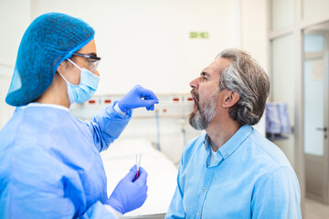 A mature Caucasian man in a clinical setting being swabbed by a healthcare worker in protective...