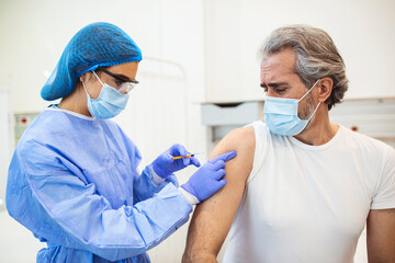 Vaccination, immunization, disease prevention concept. Man in medical face mask getting Covid-19 or flu vaccine at the hospital. Professional nurse or doctor giving antiviral injection to patient