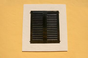 black white window with old shutters in a yellow wall, house facade