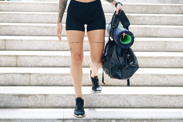 Cropped image of fit young woman in gym shorts walking down the stairs with gym bag in hands
