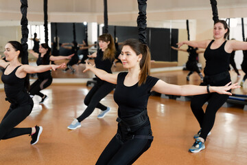 Group of active sports girls in black sportswear are engaged in budgie fitness in the gym. Bungee...