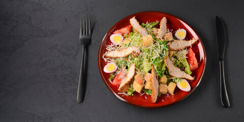 Red plate of Caesar Salad over black background. Traditional Italian cuisine concept, traditional recipe.