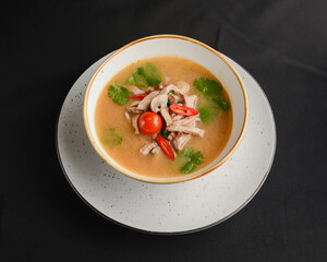 Mushroom soup of chicken broth, mushrooms, cherry tomato served in a white bowl over black background.