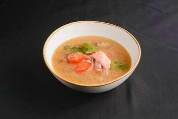 Vegetable soup with salmon in white bowl over black background. Dinner concept, healthy hot soup.