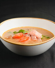Vegetable soup with salmon in white bowl over black background. Dinner concept, healthy hot soup.