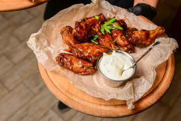 Assorted delicious grilled meat with sauce served by waiter on rustic wooden board. Restaurant service.