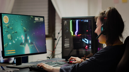 Addicted lady playing space shooter video game using headphones ,wireless joystick and RGB powerful personal computer. Cyber gamer with headset and joypad performing virtual games at gaming © DC Studio