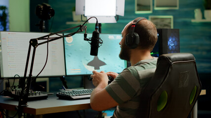 Man streamer playing space shooter video games using professional RGB keyboard and wireless joystick. Pro gamer talking into microphone on streaming chat during online tournament © DC Studio