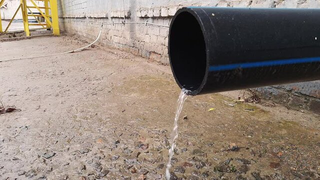 Stream of water flow from black plastic drainpipe on an industrial building at day after rain