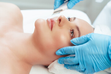 Fototapeta na wymiar Beautiful woman receiving ultrasonic face cleaning in beauty salon