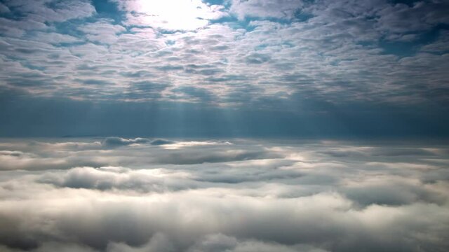 Sun shining through clouds onto flowing clouds with fog, stunning time-lapse 