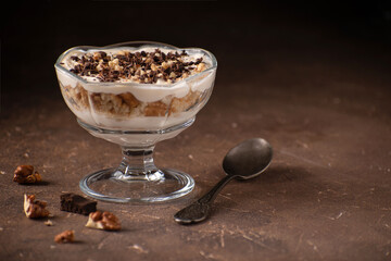 Dessert with yoghurt cream, chocolate and nuts in a glass bowl on a dark brown stone background with blank space on the right