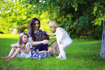 Young large family on a summer morning walk. Beautiful mother with children is playing in the park.