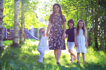 Fototapeta premium Young large family on a summer morning walk. Beautiful mother with children is playing in the park.