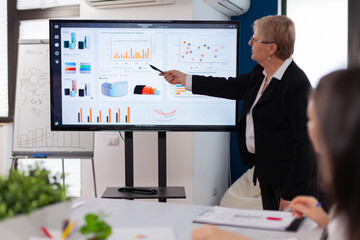 Fototapeta na wymiar Businesswoman gives talk and speaking in conference room pointing at charts briefing. Corporate staff discussing new business application with colleagues looking at screen
