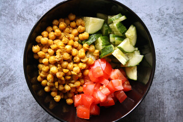 Chickpeas, tomatoes, cucumbers. Ingredients for the salad in a black bowl.