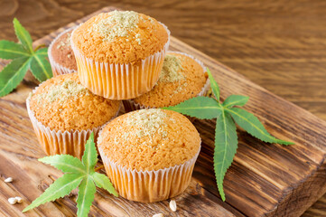Healthy and tasty vegan and gluten free muffins topped with hemp seeds on a wooden desk close-up. Marijuana cupcake muffins with cannabis leaves