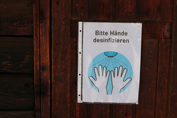 Hygiene request to disinfect hands in German at wooden door during Covid pandemic 