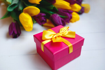 pink gift box with yellow bow on the background of a bouquet of tulips