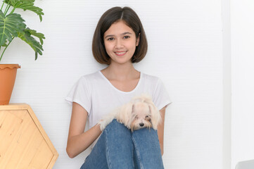 Laughing jocund young asian woman sitting on the floor with her maltese dog on knees, Cheerful and nice couple with people and pet