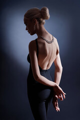 Fototapeta premium Fashion woman portrait on dark background, the silhouette woman with beautiful bent back. Naked back of woman in the dark. Luxury blonde posing in evening dress