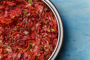 Metallic bowl of salad called Brush. Beetroot, carrots and cabbage cut into thin strips on blue wooden background. Vegetarian, organic, healthy food, diet, nutrition. Top view, copy space.