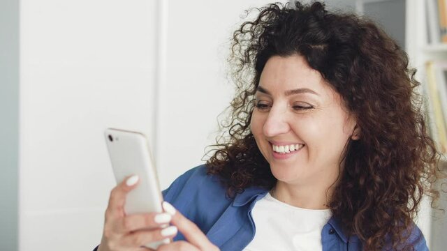 Brunette woman sincerely laughing watching funny videos or sitcom on smartphone