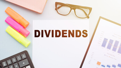 The text DIVIDENDS on office desk with calculator, markers, glasses and financial charts.